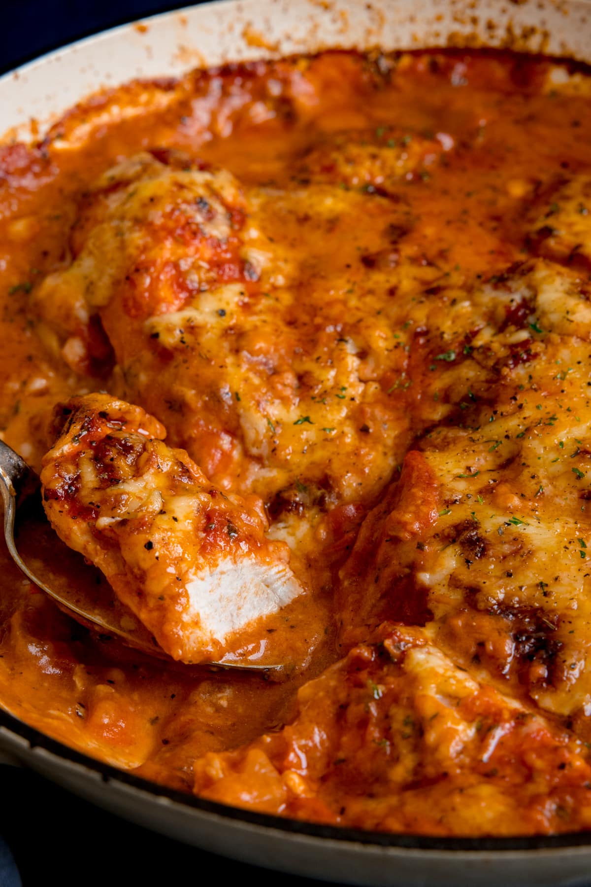 Bake chicken lasagna style in a large cast iron pan.  A spoonful of chicken is taken from the pan.